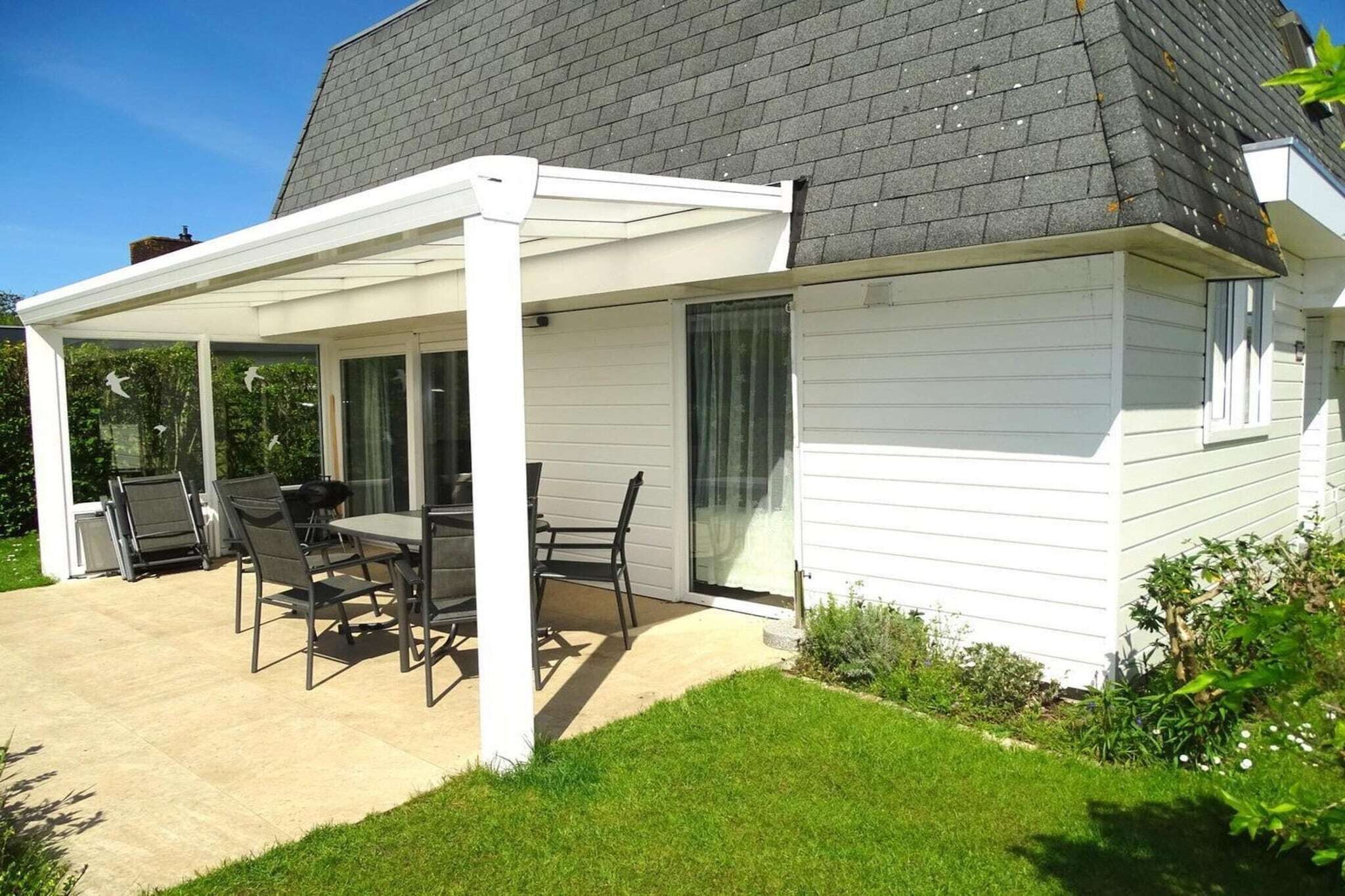 A house with a covered patio, a dining table with chairs, and a grassy yard.