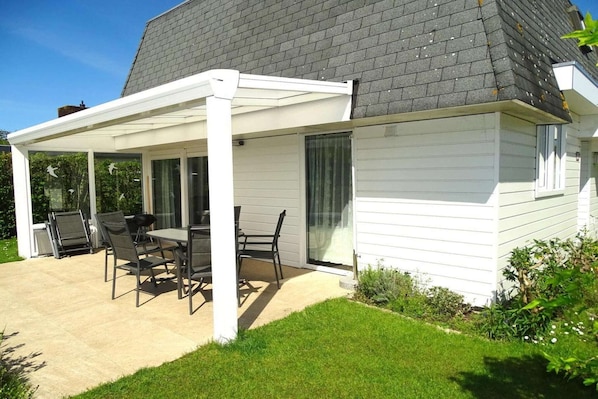 A house with a covered patio, a dining table with chairs, and a grassy yard.