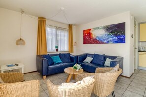 A living room with a sofa, wicker chairs, a coffee table, a painting, and a window with curtains. - House in Breskens near the Beach (Breskens)