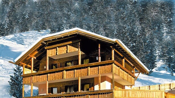 Un chalé de madera de varios pisos con balcones, con vista a una montaña nevada.