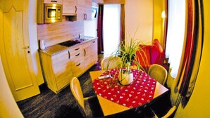 Una cocina compacta con armarios de madera y un microondas, una mesa de comedor con sillas, y una lámpara colgante.