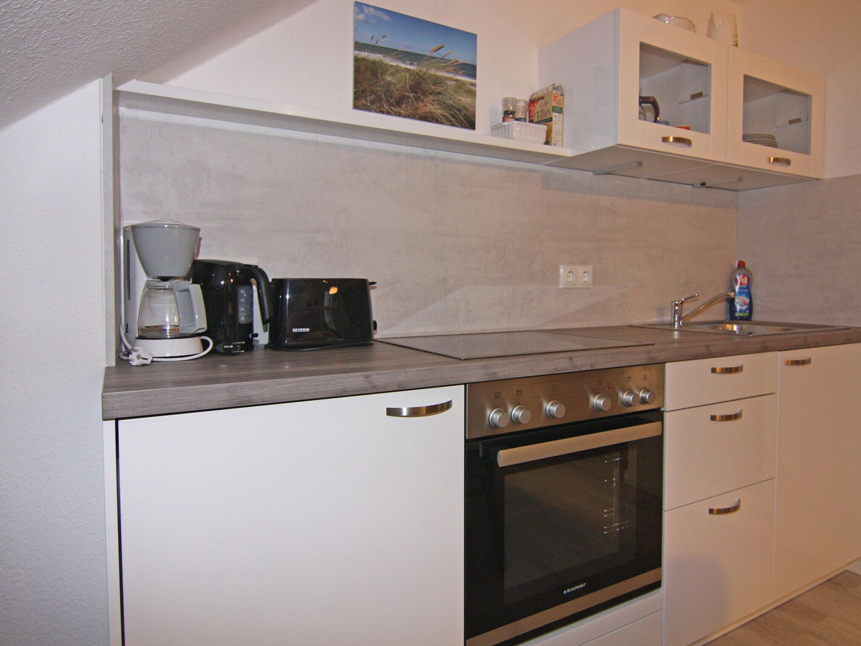 A kitchen with a coffee maker, toaster, oven, and a sink.