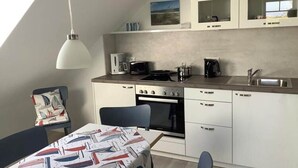Una cocina compacta con comedor, que incluye una mesa con mantel de temática náutica, una lámpara colgante moderna y armarios empotrados.