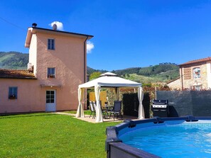 Una piscina con un gazebo bianco, un barbecue e un prato curato.