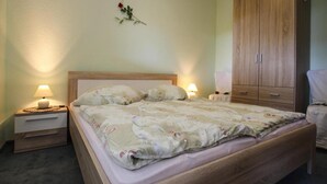 A neatly made bed with a floral comforter, two bedside tables with lamps, a wooden wardrobe, and a wall-mounted decoration. - Doppelhaushalfte, Plau am See (Plau am See)