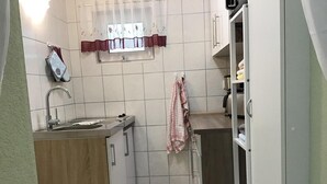 A compact kitchen with a sink, a microwave, and a small window with a curtain. - Doppelhaushalfte, Plau am See (Plau am See)