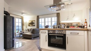 A modern kitchen with a built-in oven, a dining area with a table and chairs, and a large window providing natural light. - House by Bodden Lagoon With Sauna (Fuhlendorf)