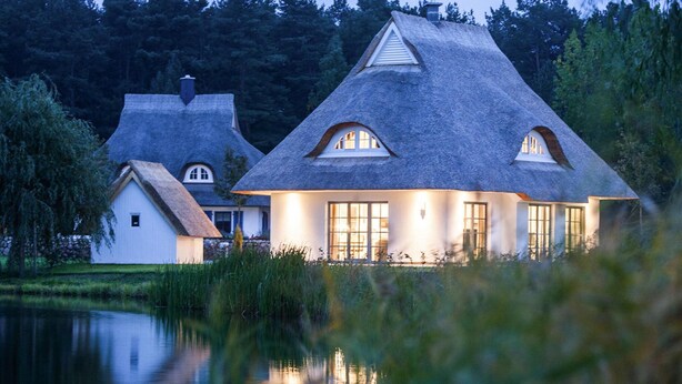 A house with a thatched roof, large windows, and a pond in the foreground. - House by Bodden Lagoon With Sauna (Fuhlendorf)