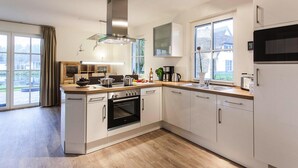 A modern kitchen with white cabinetry, a built-in oven, a microwave, and a large window offering a view of the outside. - House by Bodden Lagoon With Sauna (Fuhlendorf)