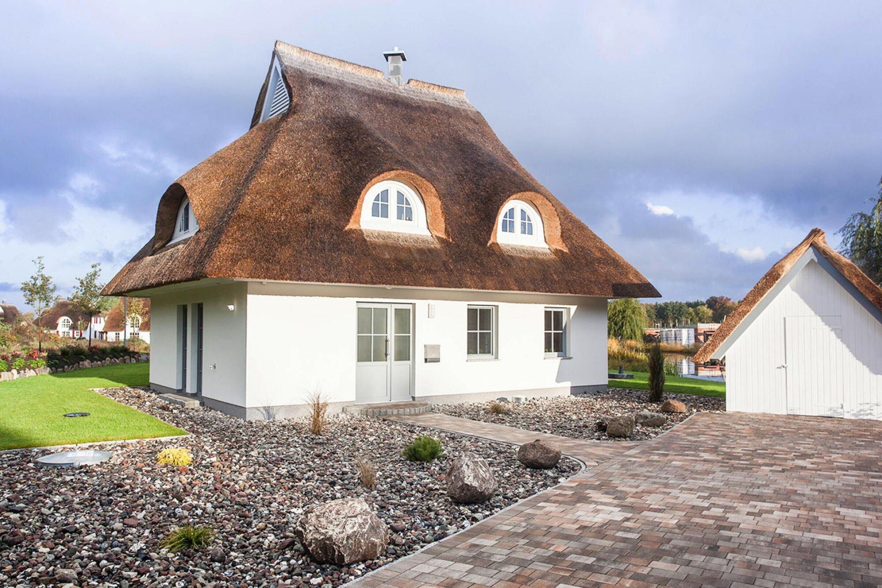 Ein modernes Haus mit geneigtem Dach, einer Haustür und einem kleinen Gartenbereich mit Steinen und Pflanzen.