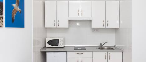 A compact kitchen with white cabinets, a microwave, a sink, and a dishwasher. There are two chairs at a table.