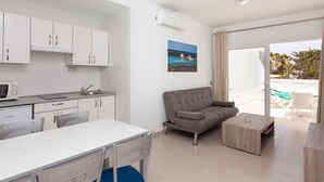 Eine moderne Küche mit weißen Schränken, ein Essbereich mit weißem Tisch und Stühlen, ein graues Sofa und ein kleiner Holztisch.