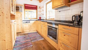 A kitchen with wooden cabinets, a stove, and a window with a red blind. - Chalet Hochkrimml With Sauna on the ski Slope (Krimml)