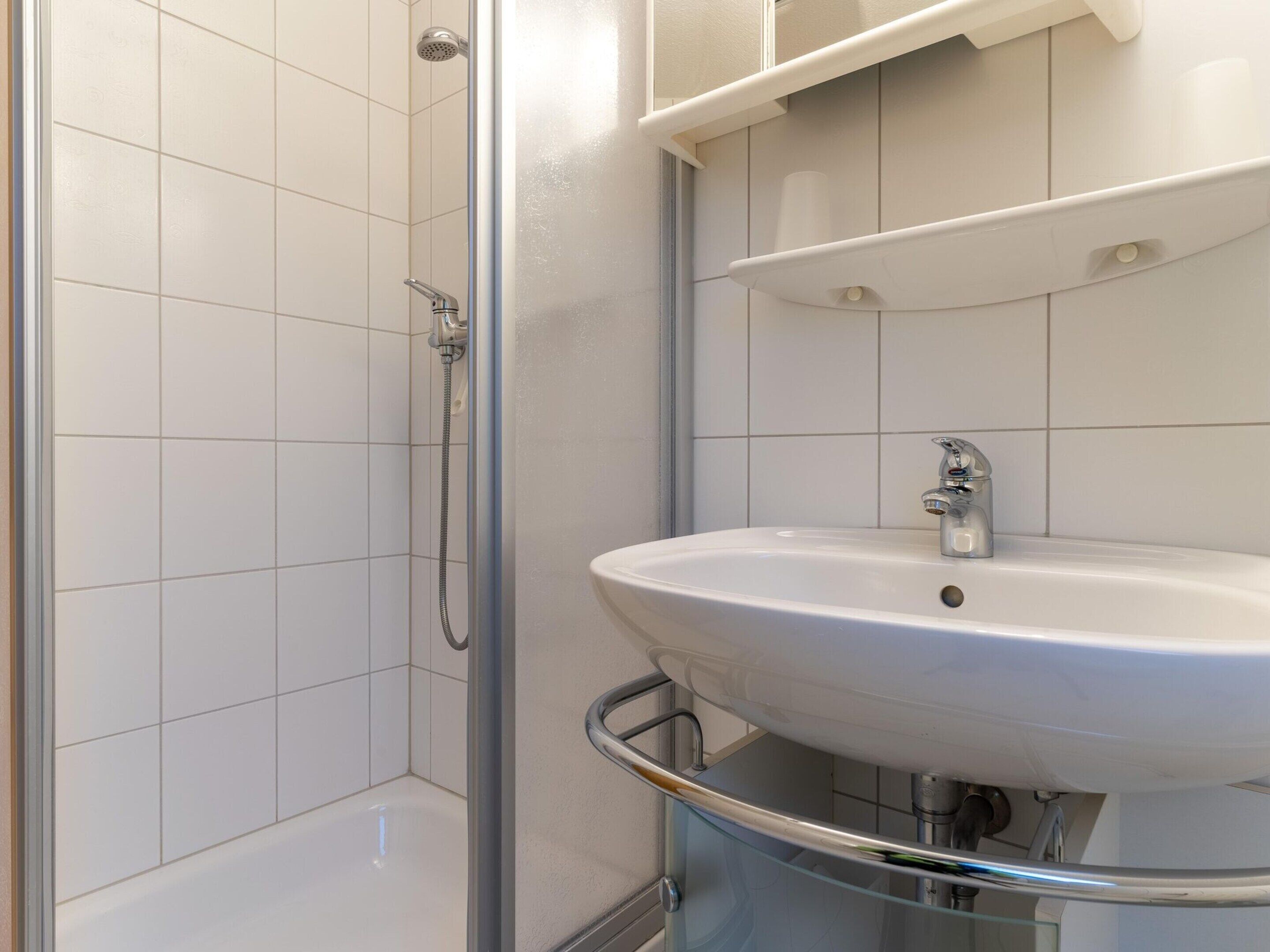 A bathroom with a glass shower enclosure, a white sink with a chrome faucet, and a white tiled wall.