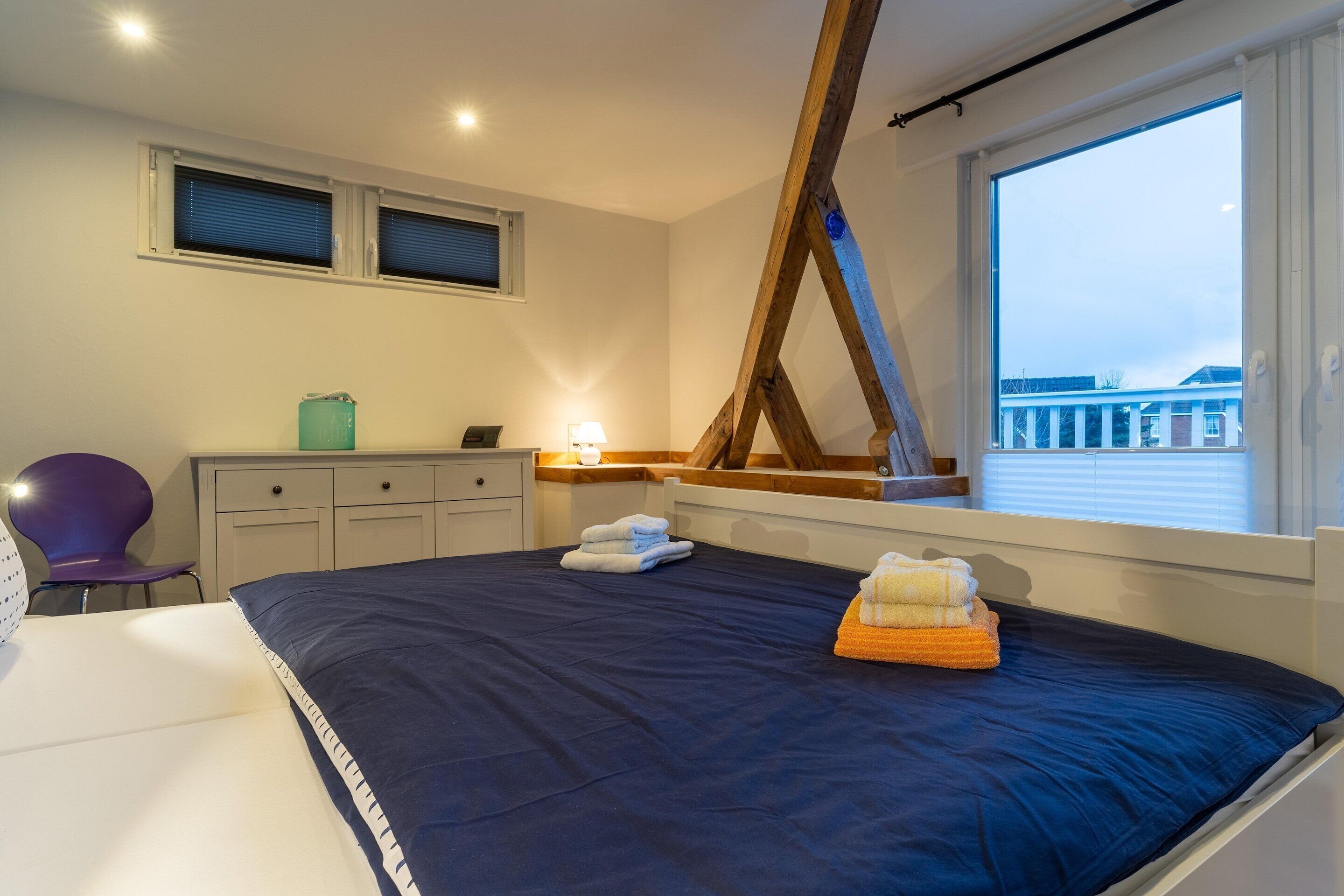 A bedroom with a large bed, a window with a view, a desk, and a chair.