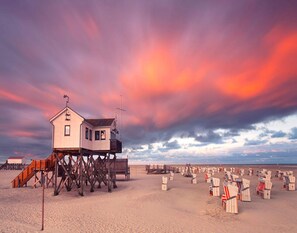 A beach house with a wooden deck and a lifeguard tower. - Wohnung in St.peter Ording (St. Peter-Ording)