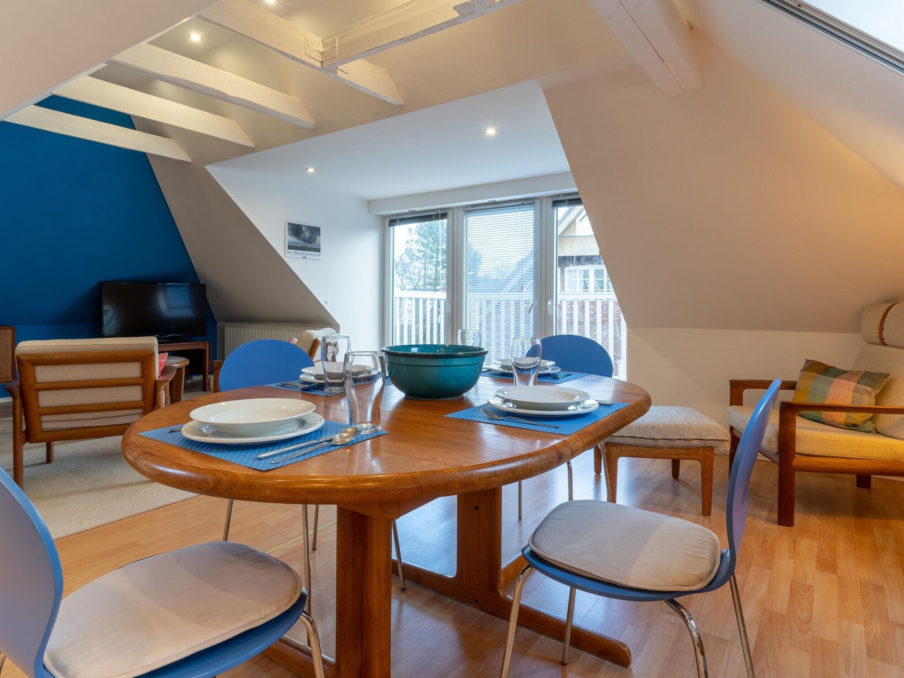 A dining area with a wooden table, blue chairs, and a large window with a view of a balcony.