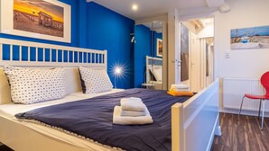 A bedroom with a bed, a nightstand, a red chair, and a painting on the wall. - Wohnung in St.peter Ording (St. Peter-Ording)
