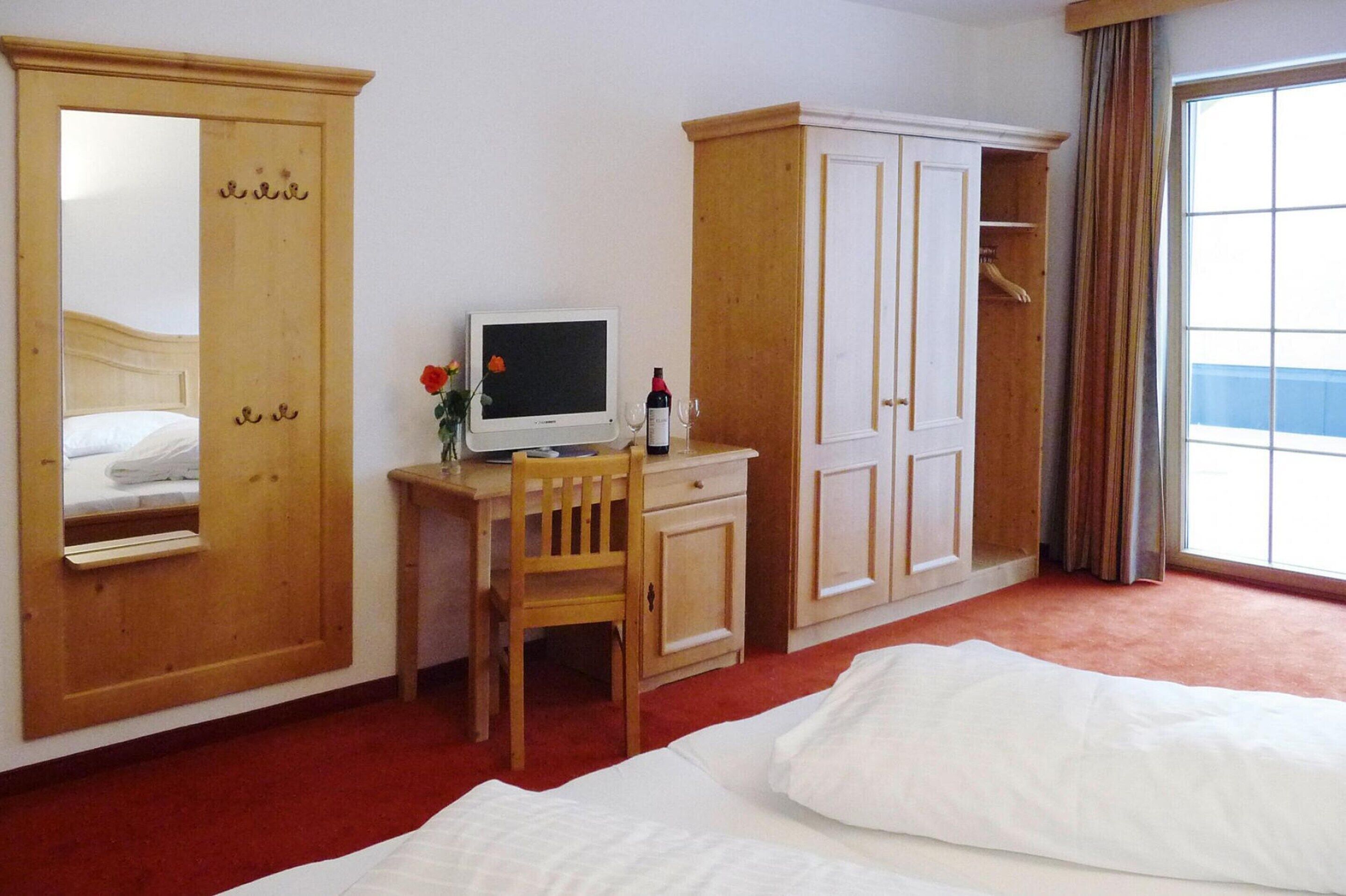 Habitació d'hotel amb un llit, escriptori amb ordinador, cadira, armari i una finestra gran.