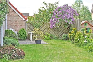 Ein Garten mit Holzzaun, kleiner Gartenhütte und verschiedenen Pflanzen und Blumen.