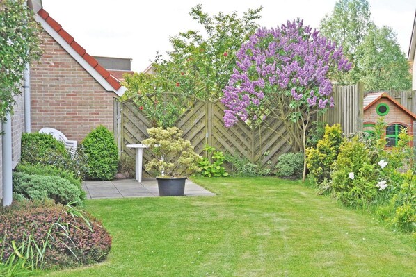 A backyard with a wooden fence, a small shed, and a variety of plants and flowers.