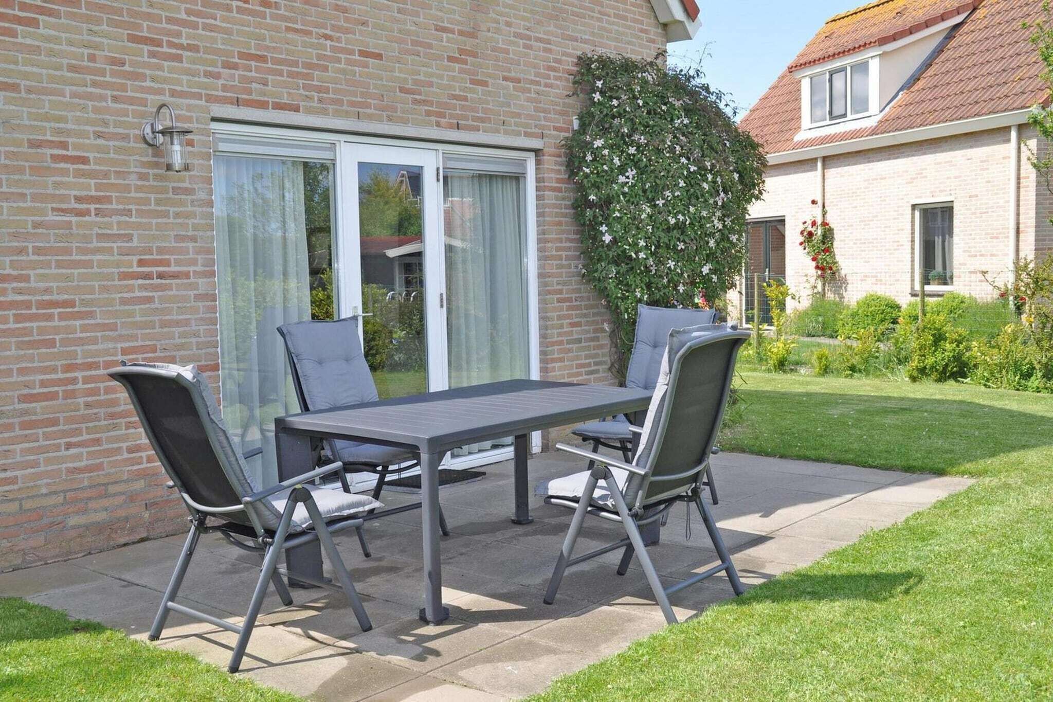 Eine Terrasse mit Tisch und Stühlen, ein Backsteinhaus und ein Garten.