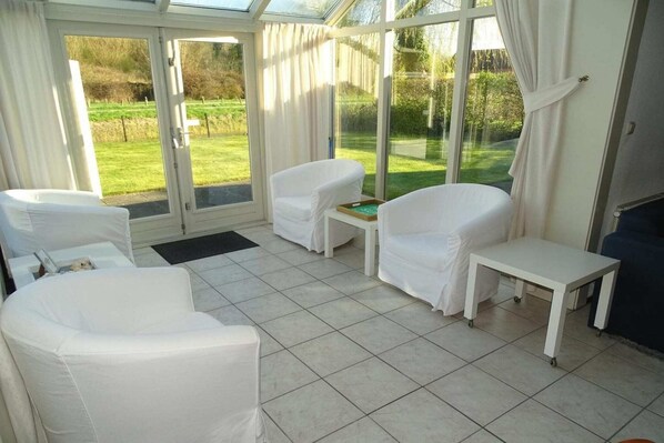 A conservatory with white furniture, a small table, and a view of a green landscape.