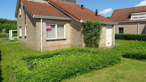 A two-story house with a red-tiled roof, a visible window with a curtain, and a sign on the door. - Bungalow in Breskens near Beach and Lighthouse (Breskens)