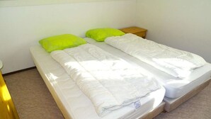 A twin bed with a white mattress and green pillows in a room with white walls and a sloped ceiling. - Bungalow in Breskens near Beach and Lighthouse (Breskens)
