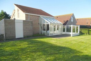 A conservatory attached to a brick house with a tiled roof, surrounded by a well-maintained lawn. - Bungalow in Breskens near Beach and Lighthouse (Breskens)