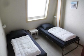 Ein kleines Zimmer mit zwei Einzelbetten, einem kleinen Tisch, einem Fenster und einem Bild an der Wand.