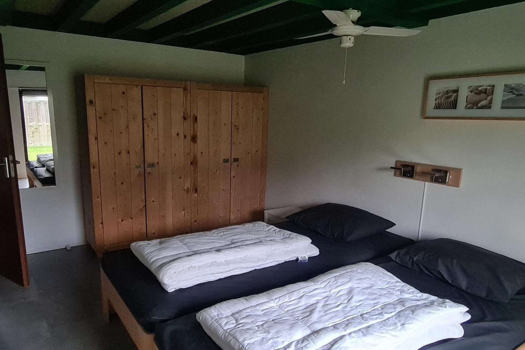 Un dormitorio con un armario de madera, una cama con ropa de cama blanca y un ventilador de techo.