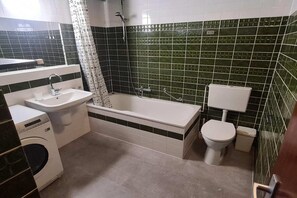 A bathroom with a bathtub, toilet, sink, and a washing machine.