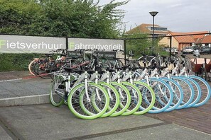 Una estación de alquiler de bicicletas con varias bicicletas, un letrero con texto y una valla.