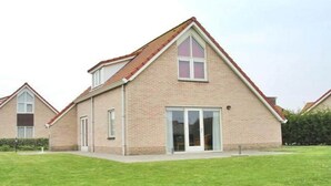 Een laag huis met bakstenen gevel, een puntgedekt dak, een voordeur en een schuifpui.