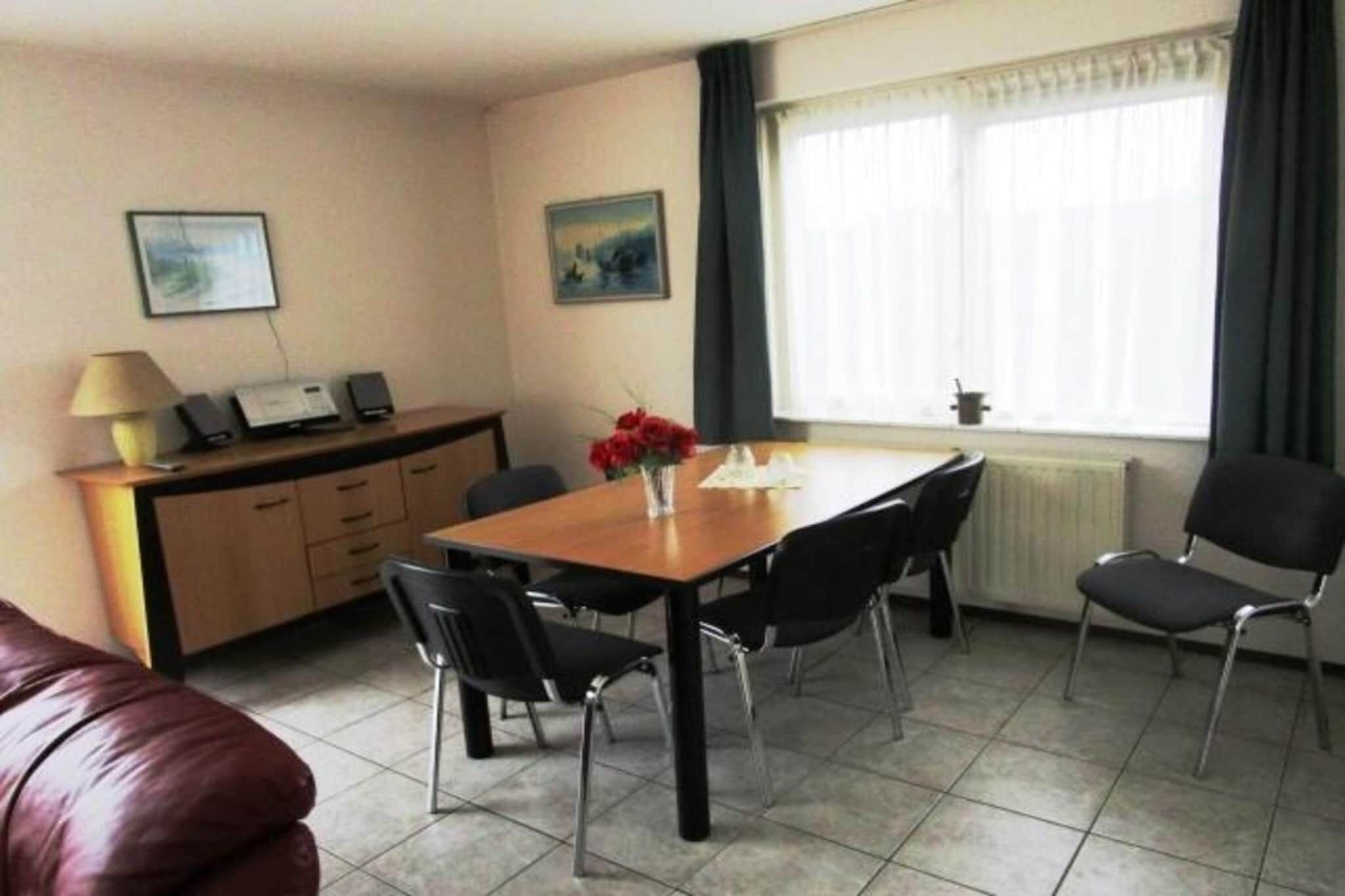 Een hotelkamer met een eettafel, stoelen, een bank, een kast met een lamp, en twee ingelijste foto's aan de muur.