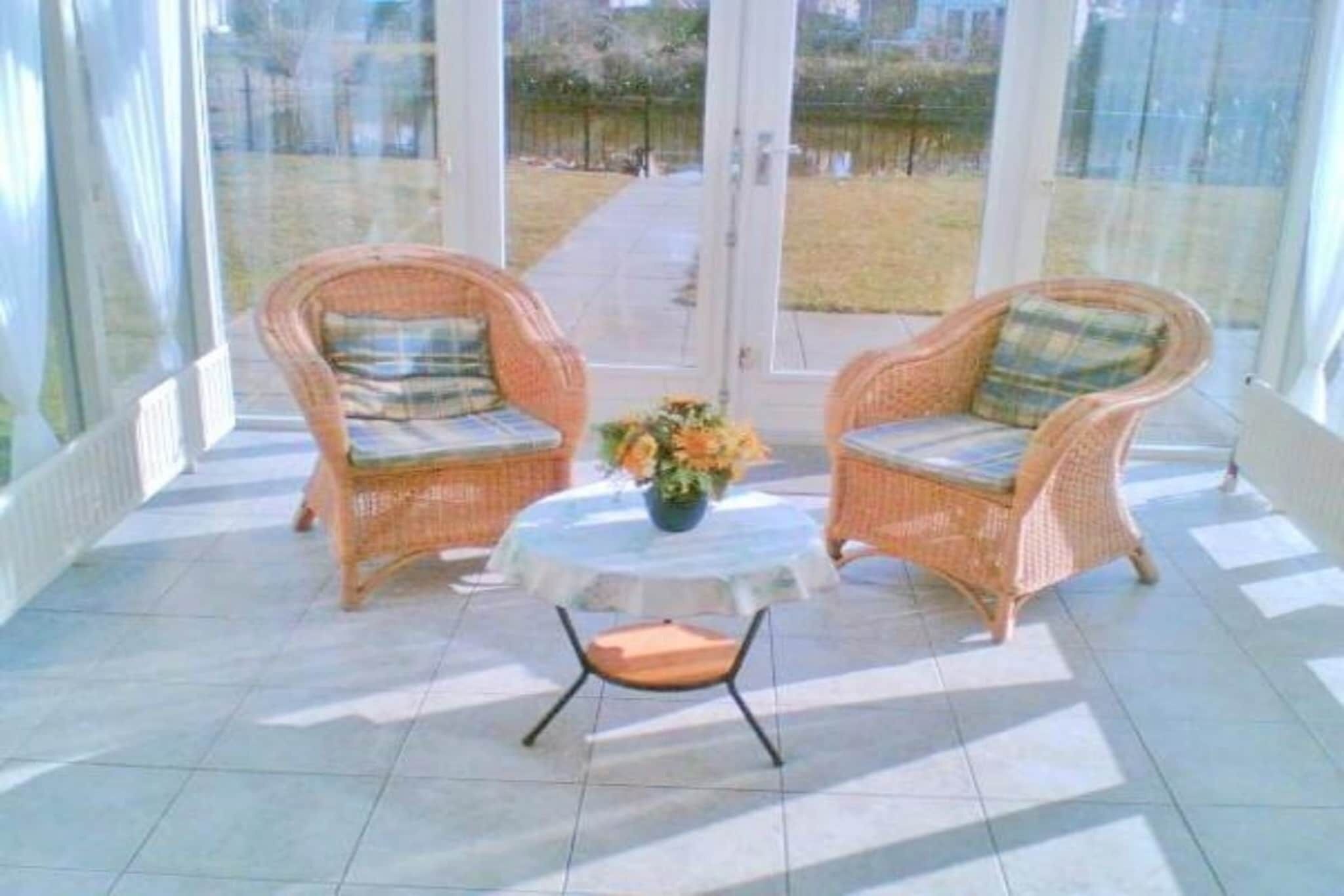 Uma área de varanda coberta com cadeiras de vime, uma mesa pequena e um vaso de flores.