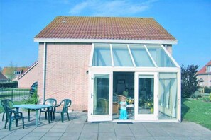 A house with a brick exterior, a tiled roof, and a glass door leading to a patio with a table and chairs.