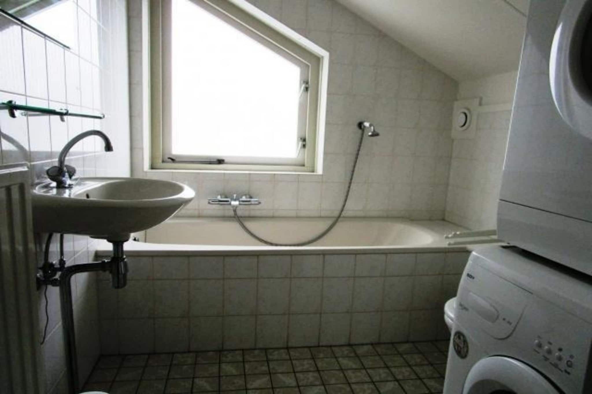 Een badkamer met een wastafel, een raam, een badkuip en een wasmachine.