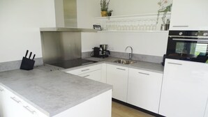 A modern kitchen with white cabinets, a stainless steel range hood, a coffee maker, and a dishwasher. - Holiday Home with Pet-Friendly Garden (Breskens)