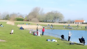 A lakeside fishing area with people fishing, chairs, and a small building in the background. - Holiday Home with Pet-Friendly Garden (Breskens)