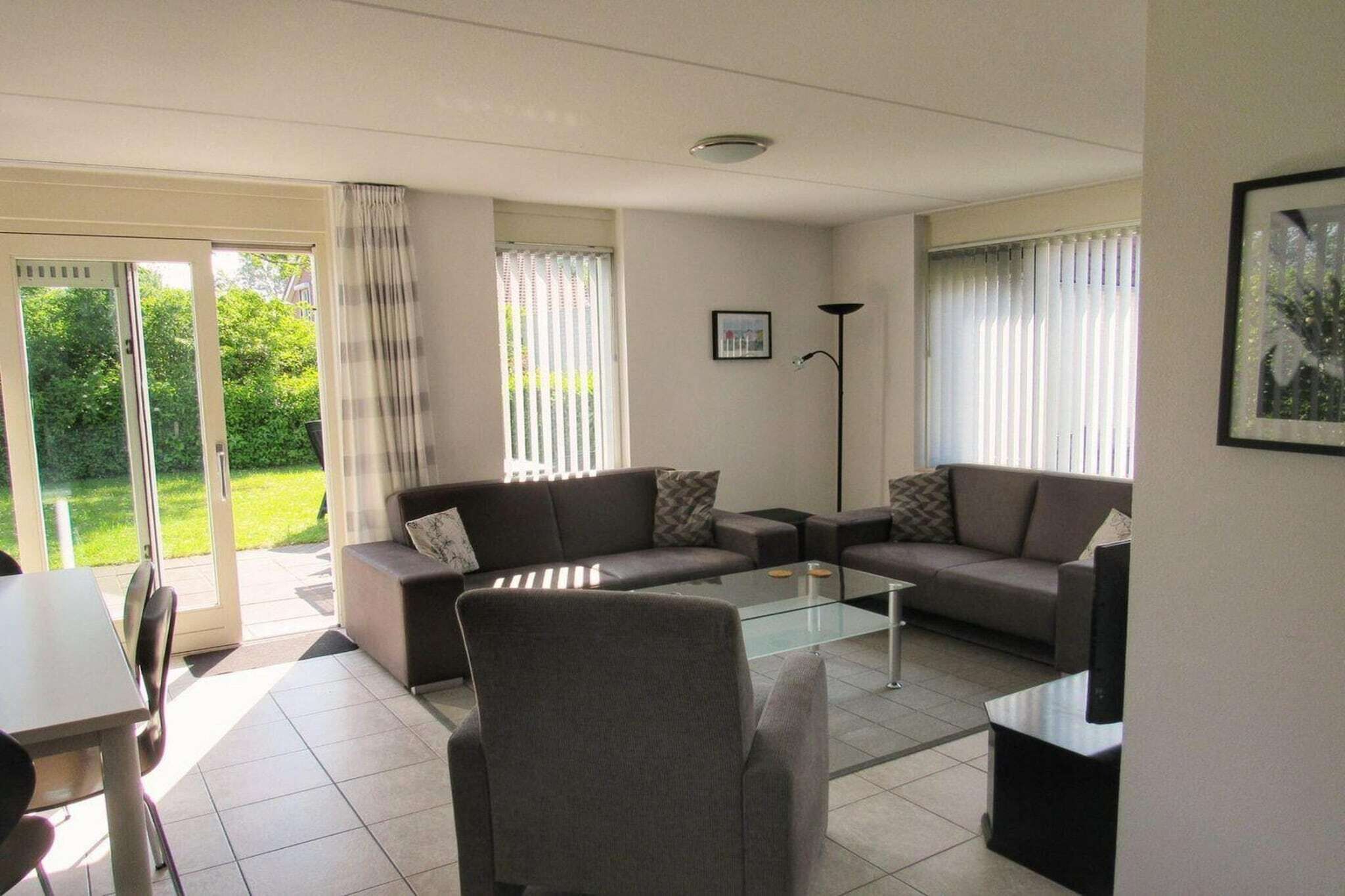 A living room with a sofa set, a coffee table, and a TV. There is a sliding glass door leading to a balcony.