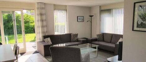 A living room with a sofa set, a coffee table, and a TV. There is a sliding glass door leading to a balcony.