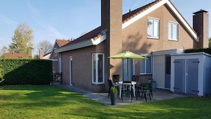 A two-story house with a brick exterior, a patio with a table and chairs, and a green umbrella.