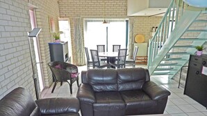 A living area with a sofa, a dining table with chairs, a staircase, and a radiator.