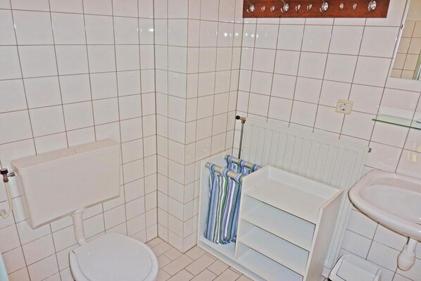 Une salle de bain avec des carreaux blancs, des toilettes, un lavabo et un porte-serviettes avec des serviettes à rayures.