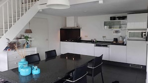 Una cocina moderna con armarios blancos, una encimera negra y un comedor con mesa y sillas negras.