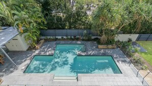 Une piscine rectangulaire avec une terrasse carrelée, entourée d’un petit muret et de différentes plantes.