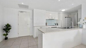Une cuisine moderne avec des meubles blancs, un îlot central doté d’un évier et une plante en pot.