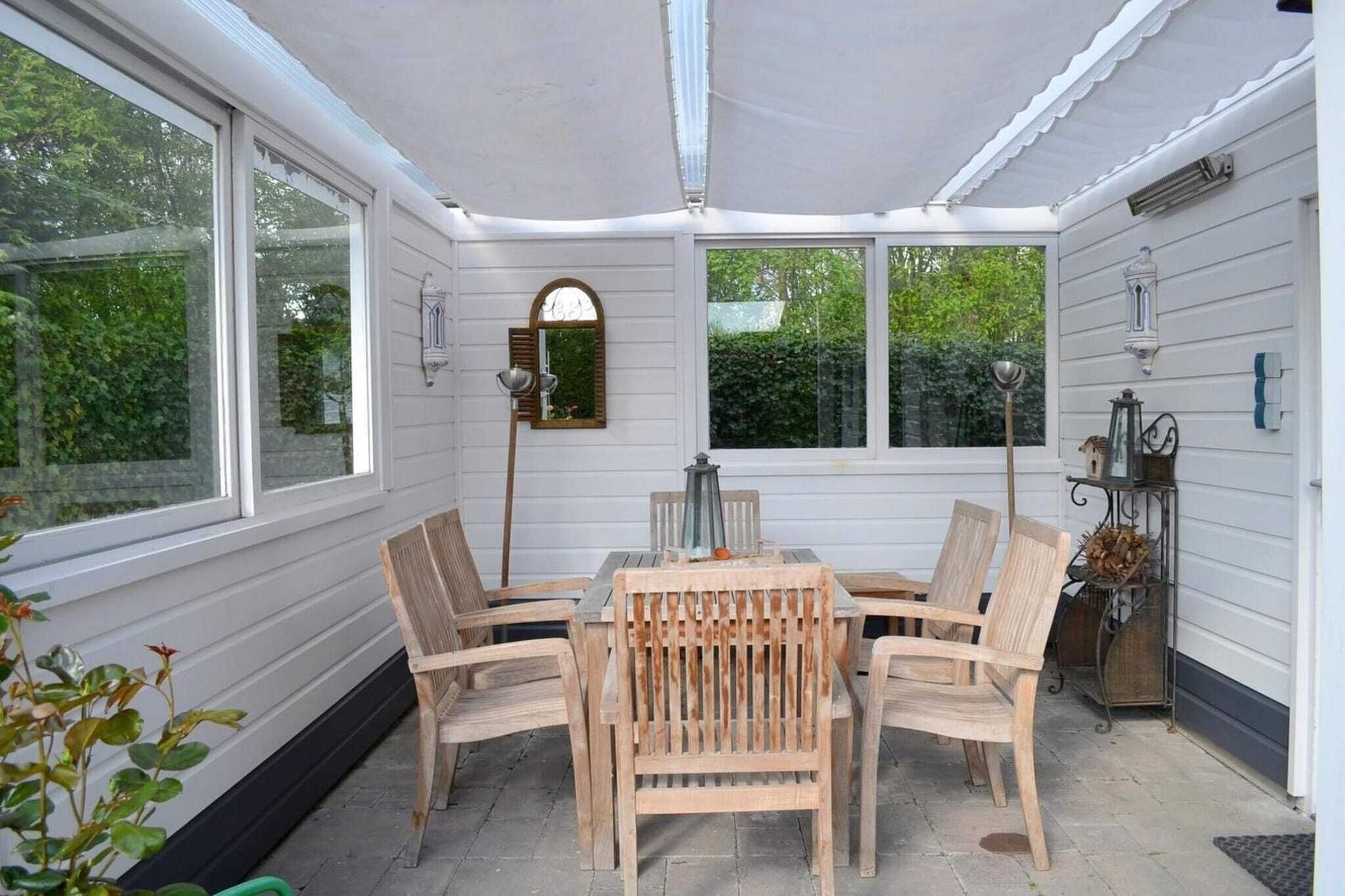 A covered patio with a table and chairs, large windows, and a lantern.